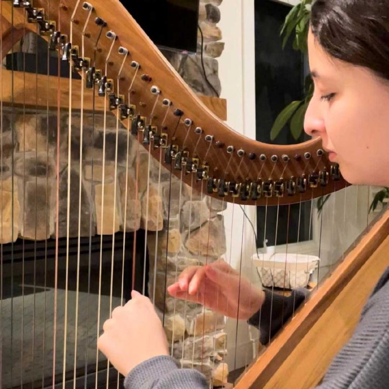 Young woman playing a harp in front of a stone fireplace