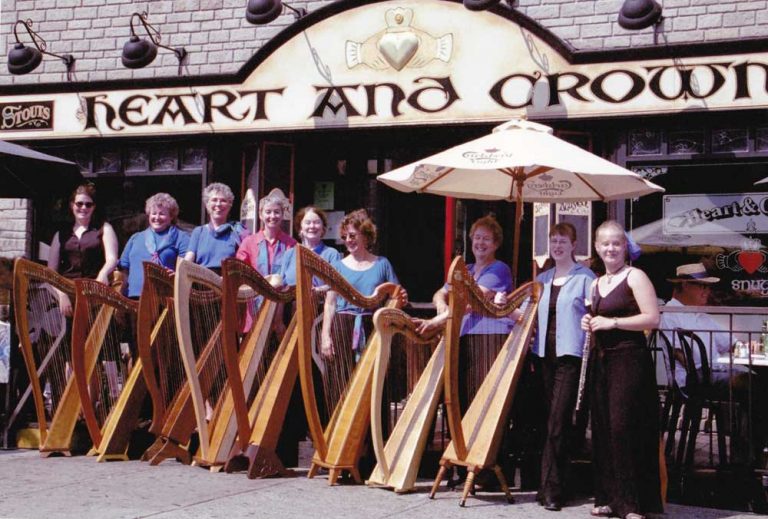 Nine members of the Ottawa Harp Choir posing with thier harps in front of the Heart and Crown Pub in Ottawa