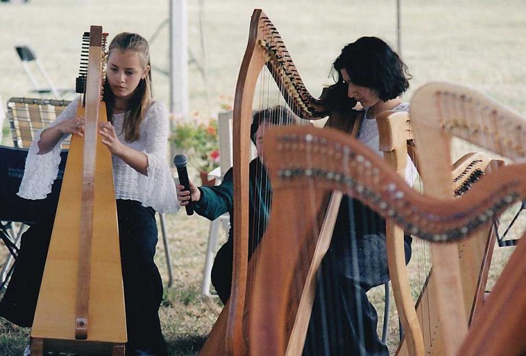 Two girls, members of the Ottawa Youth Harp Ensemble, playing. A person with a microphone is crouched behind them